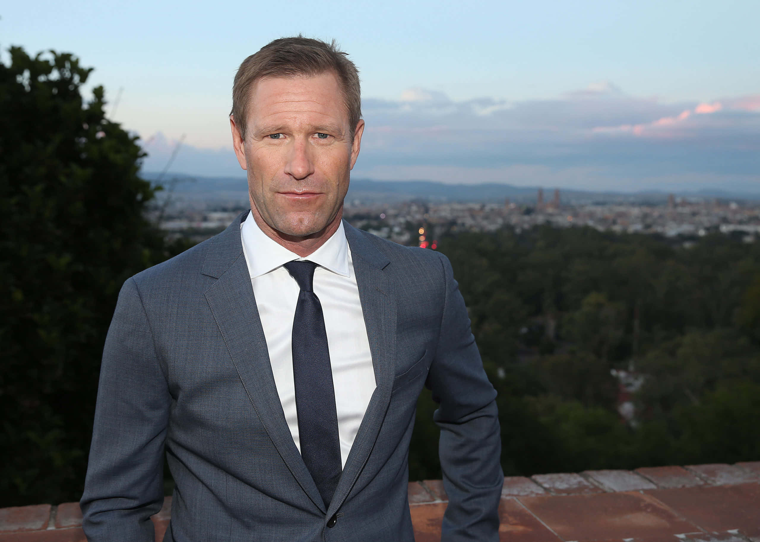 Aaron Eckhart với bầu trời xanh và thành phố Hình nền
