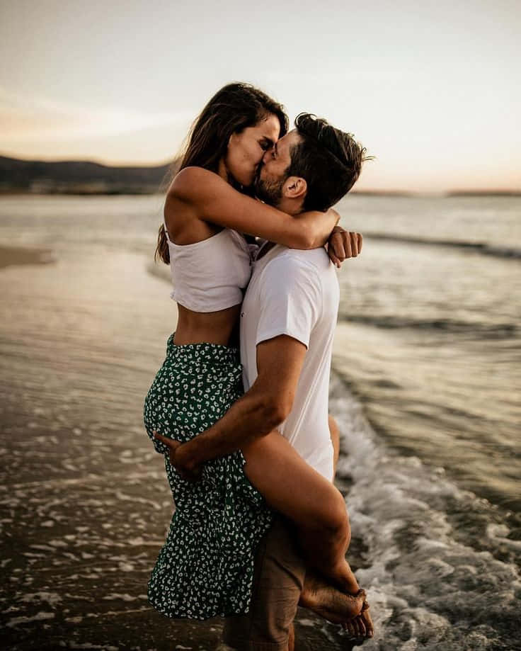 Cặp đôi trên bãi biển hôn nhau khi đang bế nhau trên sóng Hình nền