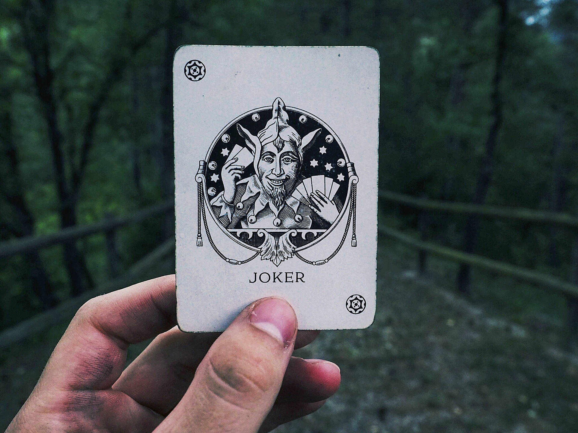 Tay cầm lá bài Joker trên nền đường quê mờ ảo.
