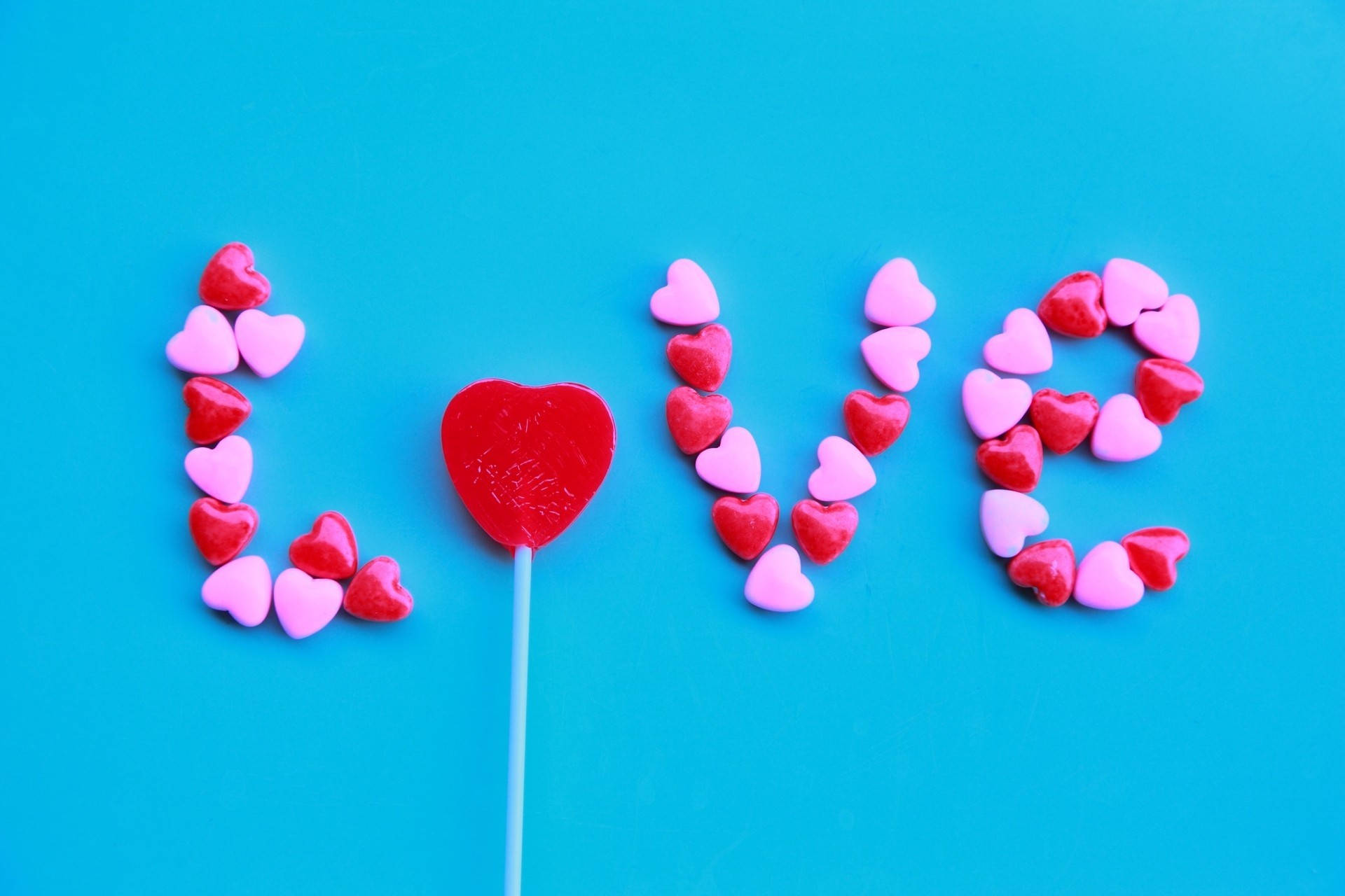 Những viên kẹo trái tim màu hồng và đỏ tạo thành chữ love trên nền tường xanh sáng dành cho Ngày lễ Tình nhân.