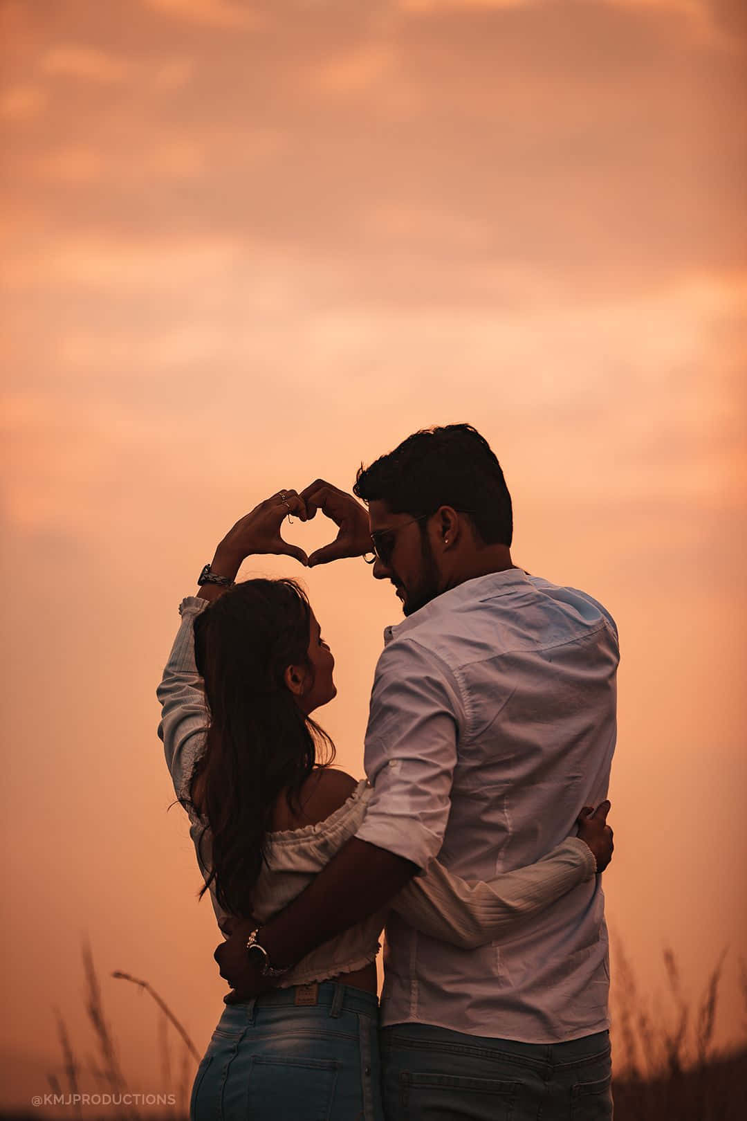 Hình ảnh đôi tình nhân tạo hình trái tim trên cánh đồng cỏ lúc hoàng hôn Hình nền