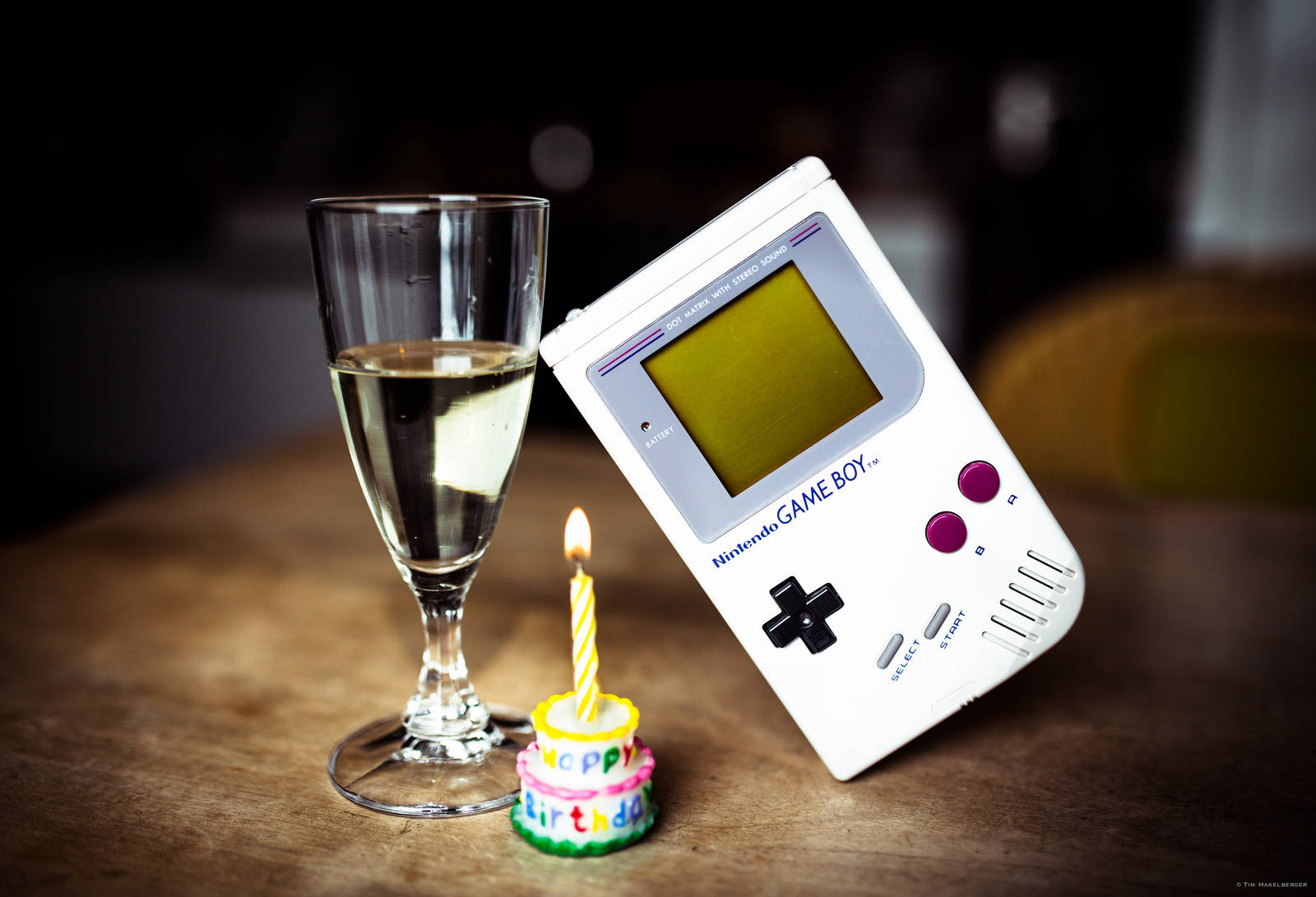 Máy chơi game Game Boy cổ điển phong cách retro đặt trên bàn kính cùng miếng bánh ngọt Hình nền