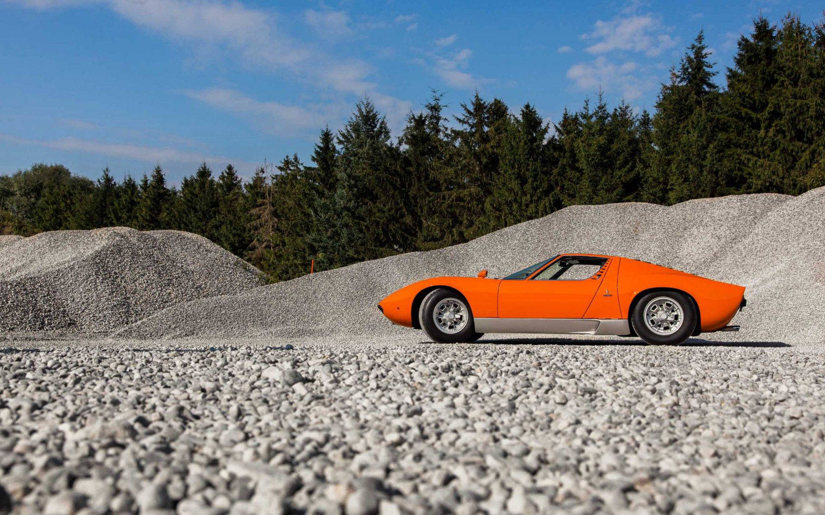 Một chiếc Lamborghini Miura cam tinh tế trên đường sỏi. Hình nền