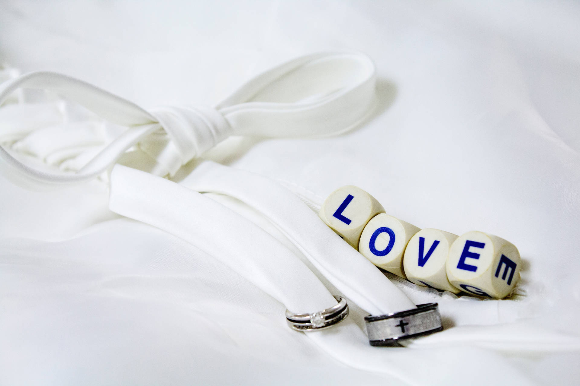 Chữ "Love" được viết trên bốn viên xúc xắc trắng bên cạnh hai chiếc nhẫn cưới bạc và đen được buộc bằng ruy băng trắng, đặt trên một tấm vải trắng.